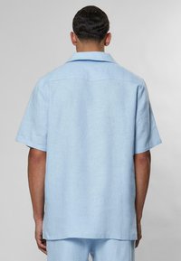Camicia a maniche corte di colore azzurro chiaro, realizzata in lino, con una vestibilità morbida, colletto aperto e un design pulito sul retro. Finitura testurizzata su tutto il capo.