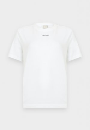 Fehér rövid ujjú, kerek nyakú póló, középen a mellkason egy kis fekete "Calvin Klein" logó, egyszínű háttér.