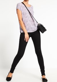 Lättviktig, mönstrad lila topp med korta ärmar, kombinerad med svarta slim-fit jeans och svarta ballerinas. Inkluderar en svart axelremsväska.