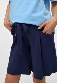 Jūras zila šorti ar mīkstu audumu, ar saitēm viduklī un sānu kabatām. Apvienoti ar gaiši zilu īsām piedurknēm topu.