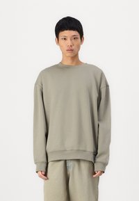 Sweatshirt vert olive clair avec des manches longues, un col rond, des poignets et un ourlet côtelés. Tissu doux avec une coupe décontractée. Design minimaliste.