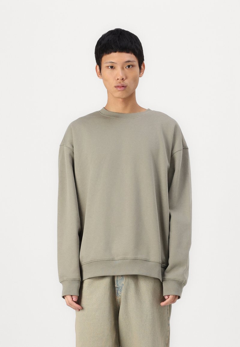 Sweatshirt vert olive clair avec des manches longues, un col rond, des poignets et un ourlet côtelés. Tissu doux avec une coupe décontractée. Design minimaliste.