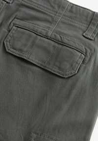 Tela de color gris oscuro, con un bolsillo de parche en la parte trasera con costuras reforzadas y una superficie suave, ligeramente texturizada.