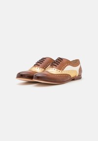 Brune og gull lær wingtipsko med høyglansfinish, med broguedetaljer og svarte snører. Glatt tekstur med kontrastakenter.