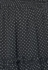 Černá tkanina s bílými puntíky, s nařasenou texturou a volánovým krajkováním. Materiál vypadá lehce a měkce.