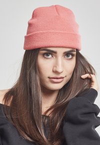 Strikket rosa lue med brettet kant, som har en ribbestruktur og tett passform, kombinert med en svart off-shoulder topp.