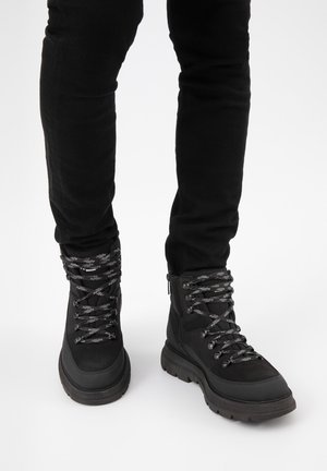 Czarne buty trekkingowe o teksturowanym wykończeniu, z pięcioma parami oczek i grubymi czarnymi sznurówkami. Solidna podeszwa dla lepszej przyczepności.