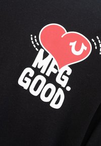 Rotes Herz mit weißem Hufeisen oben über weißem Text "MFG. GOOD" auf schwarzem Stoff, mit dekorativen gestrichelten Linien um das Herz.