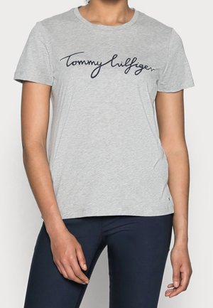 Camiseta de algodón gris claro con un logo en cursiva azul marino "Tommy Hilfiger" en el pecho. Cuello redondo clásico y mangas cortas.