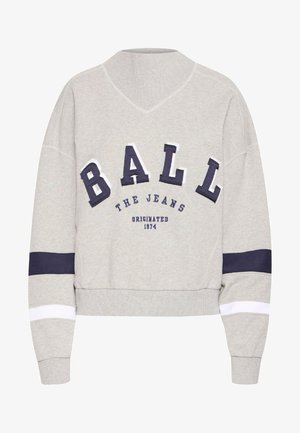 Grå genser med V-hals, med overdimensjonerte marineblå og hvite bokstaver og striper på ermene. Stoffet har en myk tekstur.
