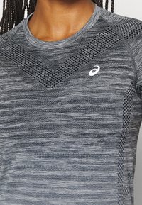 Camisa atlética gris con tejido texturizado y un diseño de malla en los hombros, además de un logo de Asics en blanco en la parte superior izquierda.