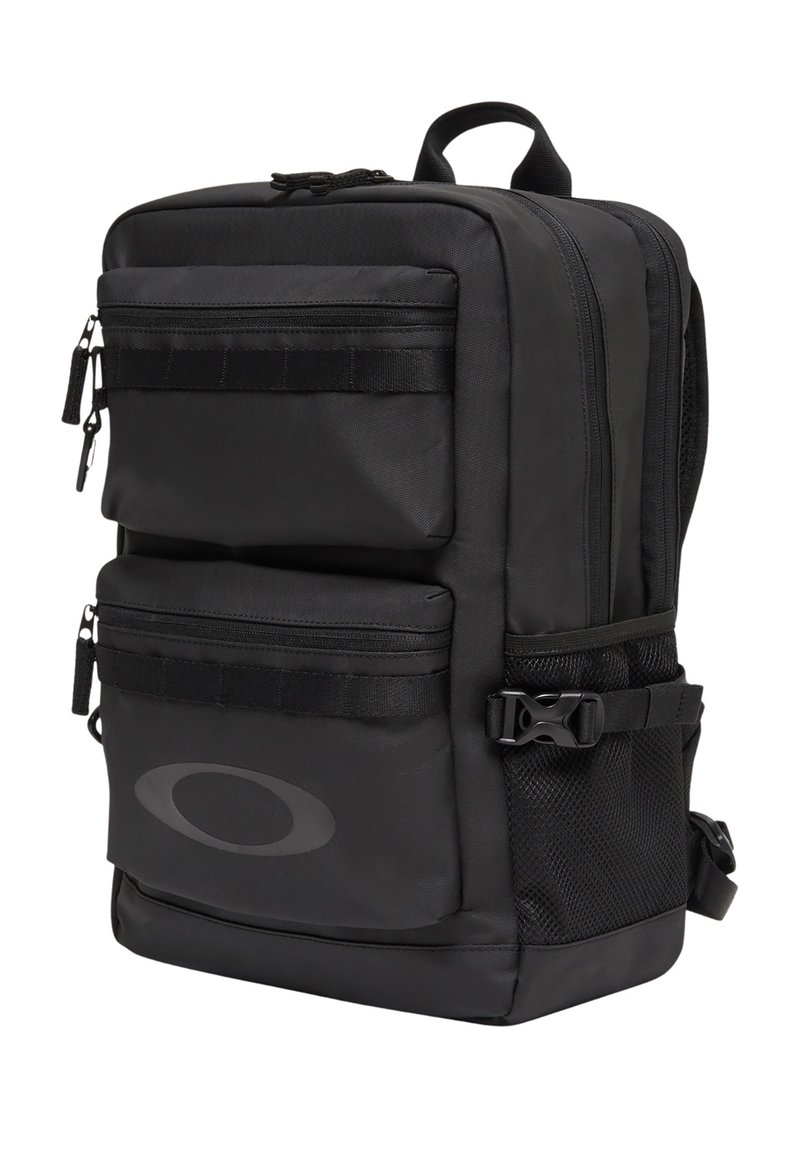 Sac à dos rectangulaire noir avec deux poches avant zippées, poche latérale en mesh, poignée supérieure, bretelles réglables et logo ovale discret sur la poche avant inférieure.