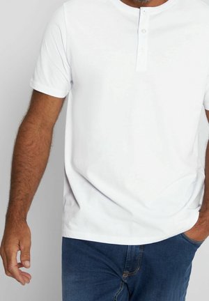 Biała koszula henley z krótkim rękawem i trzema guzikami, wykonana z gładkiej bawełny, połączona z niebieskimi dżinsami.