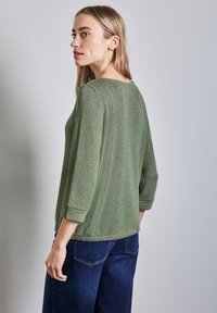 Zelený textured svetr s širokým výstřihem, tříčtvrtečními rukávy a rovnými lemy, doplněný tmavými džínami s vysokým pasem.