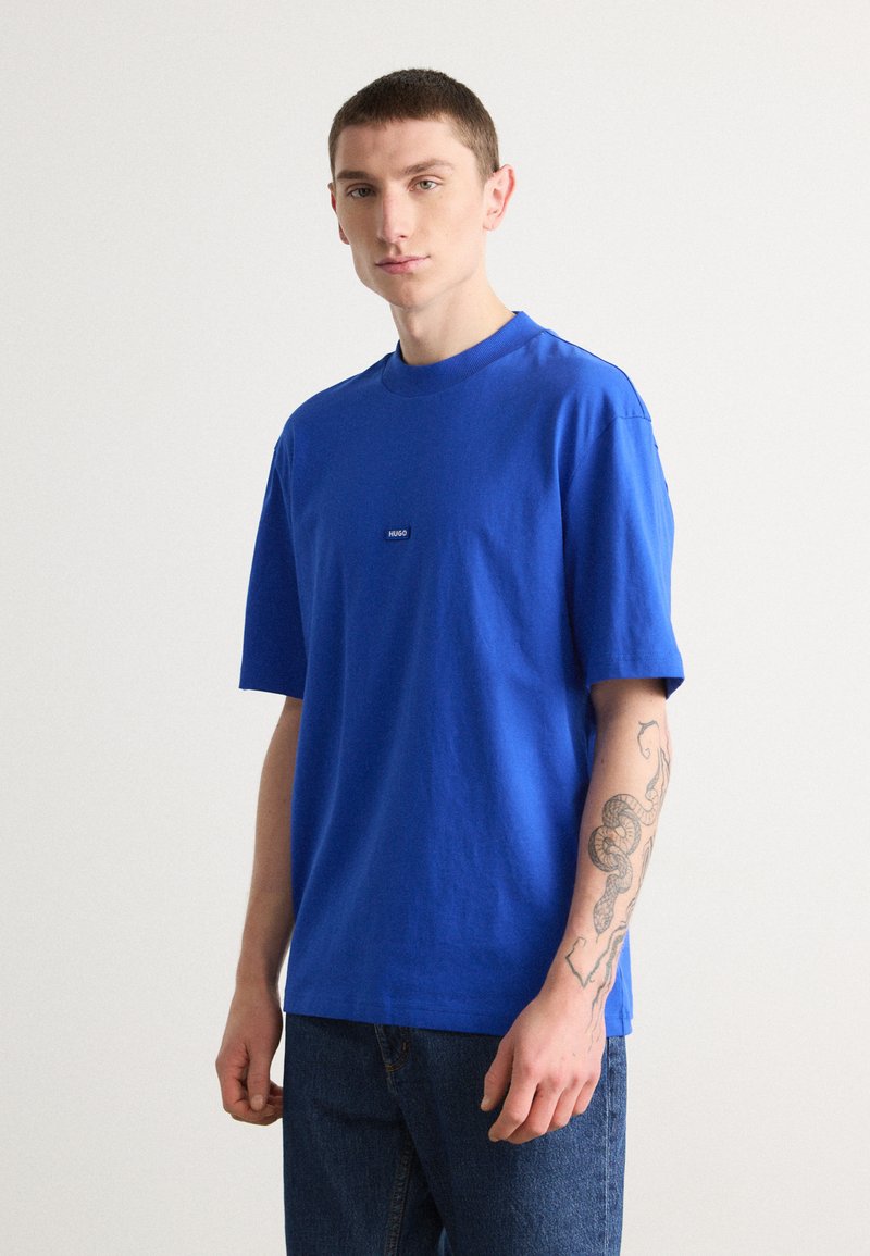Blå bomulls t-skjorte med rund hals og korte ermer, med et lite logo-lapp på brystet, kombinert med blå jeans.