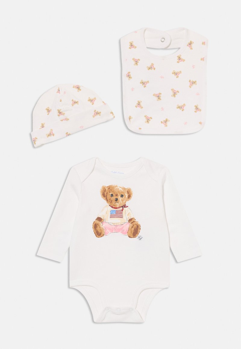 Biely bavlnený detský overal s grafickým vyobrazením medvedíka, dlhé rukávy, ružové akcenty, plus zodpovedajúca detská podbradník a čiapka s potlačou medvedíka.