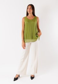 Top verde senza maniche con scollo a barca, realizzato in un tessuto fluido. Abbinato a pantaloni bianchi a gamba larga e décolleté neri a punta.