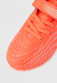 Ποδοσφαιρικό παπούτσι σε πορτοκαλί χρώμα με υφασμάτινο συνθετικό επάνω μέρος με υφή, διακοσμημένο με μικρές λευκές κουκκίδες, και στερεώνεται με κορδόνια και ιμάντα με βέλκρο.
