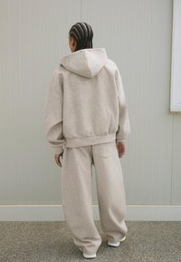 Bež hoodie s kapuljačom i rebrastim manžetama, uparen s labavim bež trenirkama. Mekana tkanina s mat površinom, minimalni šavovi.
