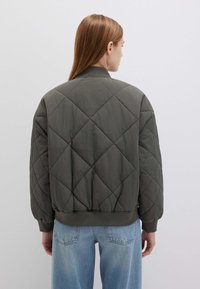 Giacca bomber trapuntata in verde oliva, realizzata in tessuto leggero con polsini e orlo a costine, caratterizzata da una vestibilità ampia e un motivo a diamante.