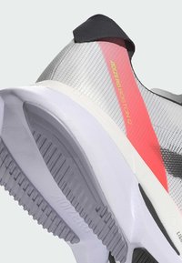 Zapatillas de running Adizero Boston 12 con parte superior de malla translúcida en gris, acentos en un rosa brillante, media suela blanca acolchada y suela exterior texturizada en gris.
