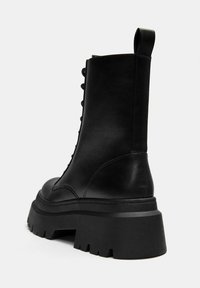 Fekete bőr bokacsizma, vastag platform talppal, fűzős elejével és könnyű felhúzást segítő húzószalaggal a saroknál.