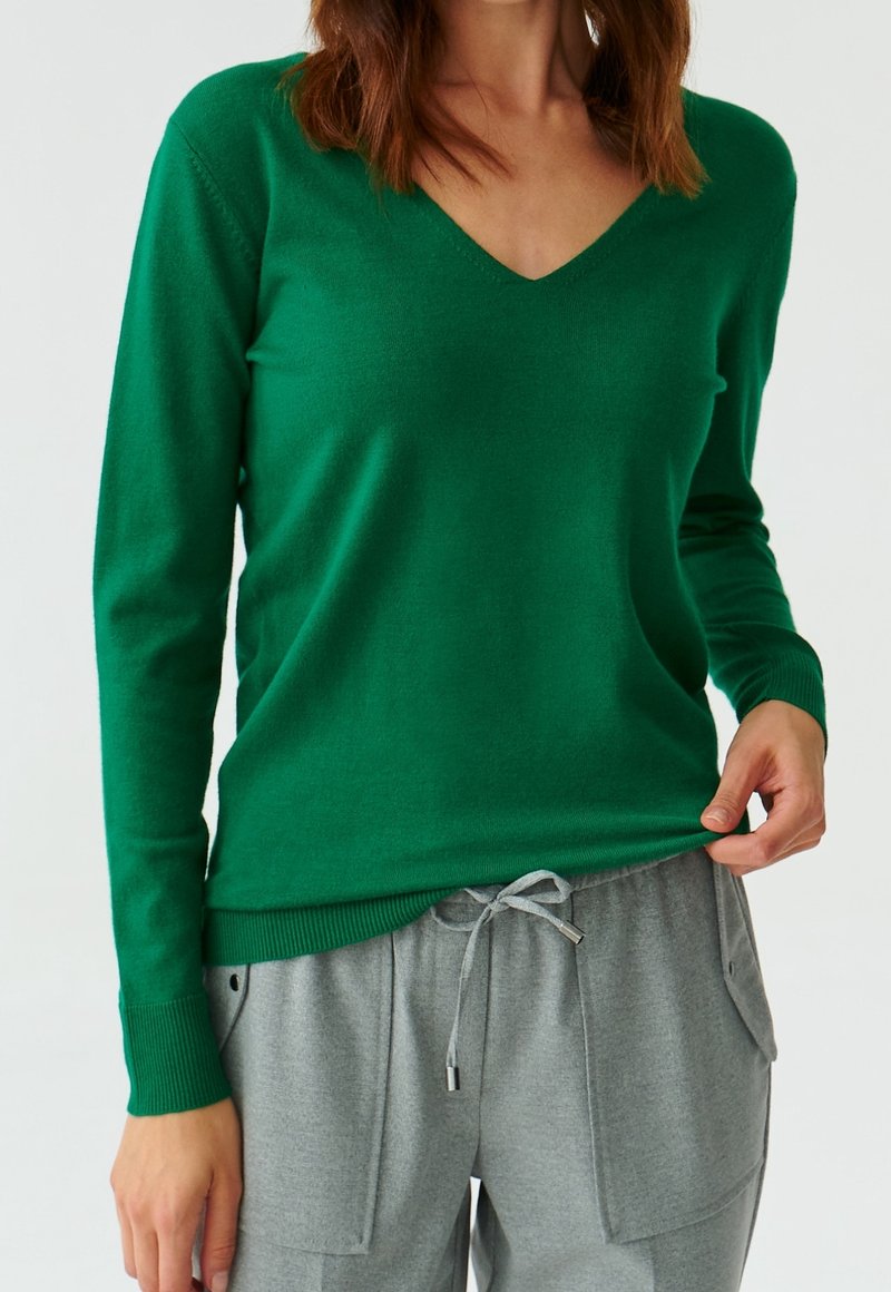 Maglione verde a scollo a V con maniche lunghe, tessuto morbido e polsini a costine, abbinato a pantaloni sportivi grigi con coulisse e tasche applicate.
