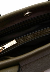 Intérieur de sac à main vert olive avec quincaillerie dorée, doté d'une poche zippée et d'une doublure en tissu texturé. Plusieurs compartiments visibles.