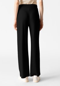 Pantaloni larghi neri a pieghe realizzati in tessuto leggero, con una vita alta, dalla texture liscia e dettagli in sneakers bianche.