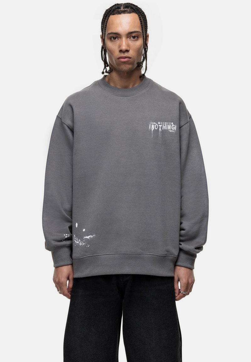 Grijze sweatshirt met een ronde halslijn, drop shoulders, bedrukt tekst en spetters bij de zoom. Zacht materiaal met een losse fit.