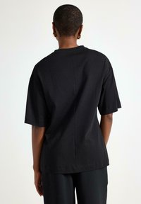 T-shirt nera a maniche corte con vestibilità rilassata, caratterizzata da una scollatura rotonda e da un dettaglio con cucitura centrale sul retro. Realizzata in morbido tessuto di cotone.