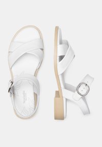 Sandales en cuir blanc avec un design à brides croisées, boucle réglable à la cheville et un petit talon carré beige. Semelle intérieure texturée avec un motif à pois.