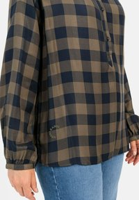 Lange mouw knoopshirt in een bruin en marineblauwe ruitpatroon, met een afgeronde zoom, elastische manchetten en een logo-detail aan de zijkant.