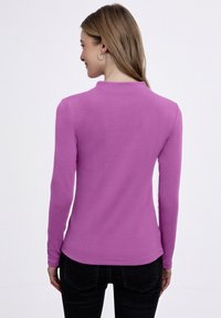 Maglietta a maniche lunghe in tessuto rosa vivace, con scollatura rotonda e silhouette aderente, abbinata a pantaloni neri.