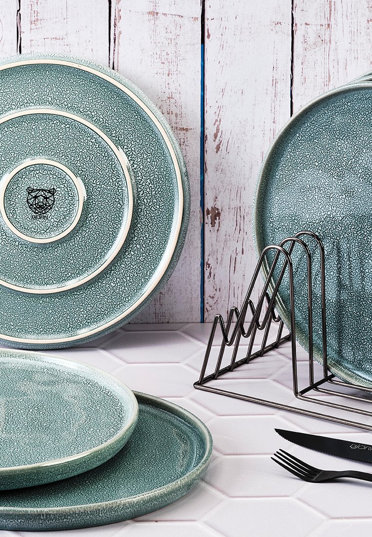 Set aus drei runden, strukturierten Tellern in Türkis mit weißen Rändern, die ein Logo zeigen. Begleitet von einem Metalltellerhalter und schwarzem Besteck.