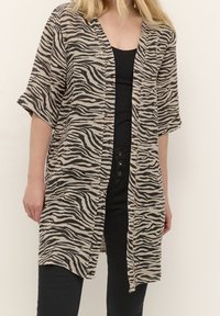 Kimonon, joka on tehty beige-mustasta kankaasta ja jossa on seeprahärmäkuvio. Sen leikkaus on väljä, leveät hihat ja avoin etuosa.