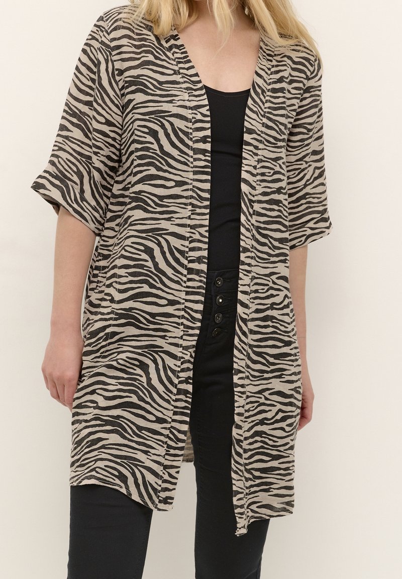 Kimonon, joka on tehty beige-mustasta kankaasta ja jossa on seeprahärmäkuvio. Sen leikkaus on väljä, leveät hihat ja avoin etuosa.