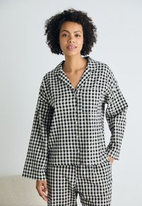 Svart och vit rutmönstrad pyjamasuppsättning i lätt material; har knäppning med knappar, krage och långa ärmar med avslappnad passform.