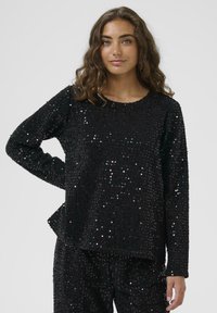 Maglietta nera a maniche lunghe con vestibilità ampia, ricoperta di paillettes brillanti, con scollatura rotonda e orlo piatto, abbinata a pantaloni coordinati.