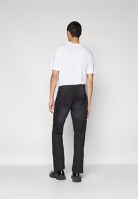 Pantalones cargo negros con múltiples bolsillos, combinados con una camiseta blanca lisa. El material parece duradero y ligeramente texturizado; el calzado es negro y de suela gruesa.