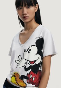 Camiseta de algodón blanca con un gran gráfico de Mickey Mouse en negro y rojo con acentos amarillos; diseño de cuello en V.