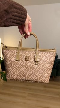 Small beige handbag with a textured pattern, dual top handles, and a gold-tone logo accent on the front. Features a zipper closure.