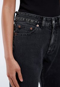 Black denim jeans feature a high waist, five-pocket design, copper-tone hardware, and subtle fading along the fabric texture.
