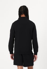 Zwarte sweatshirt met een hoge kraag, geribbelde manchetten en tailleband, gemaakt van een zacht materiaal; heeft een klein zakje op de bovenrug.