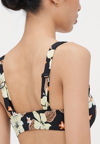 Čierny kvetinový bikiny top s veľkými žltými a oranžovými hibiskusovými motívmi. Nastaviteľné ramienka s kovovými detailmi. Hladká textúra látky.