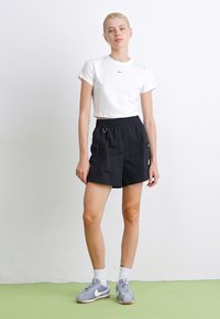 White cropped t-shirt with a small logo, paired with black athletic shorts featuring a drawstring waist and side pockets, complemented by gray sneakers.