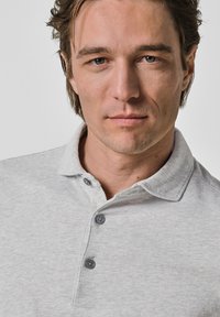 Graues Polohemd mit klassischem Kragen, ausgestattet mit drei dunklen Knöpfen, hergestellt aus einem glatten Stoff mit feiner Textur.