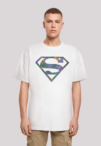White cotton t-shirt featuring a colorful floral-patterned Superman logo in purple, orange, and green. Relaxed fit with short sleeves.