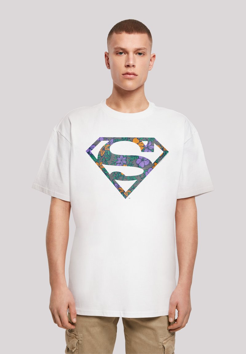 White cotton t-shirt featuring a colorful floral-patterned Superman logo in purple, orange, and green. Relaxed fit with short sleeves.
