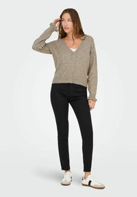 Ljusbrun stickad kofta med V-ringning, knäppning med knappar, diamantmönster, ribbade muddar, ihopparad med svarta skinny jeans och sneakers.